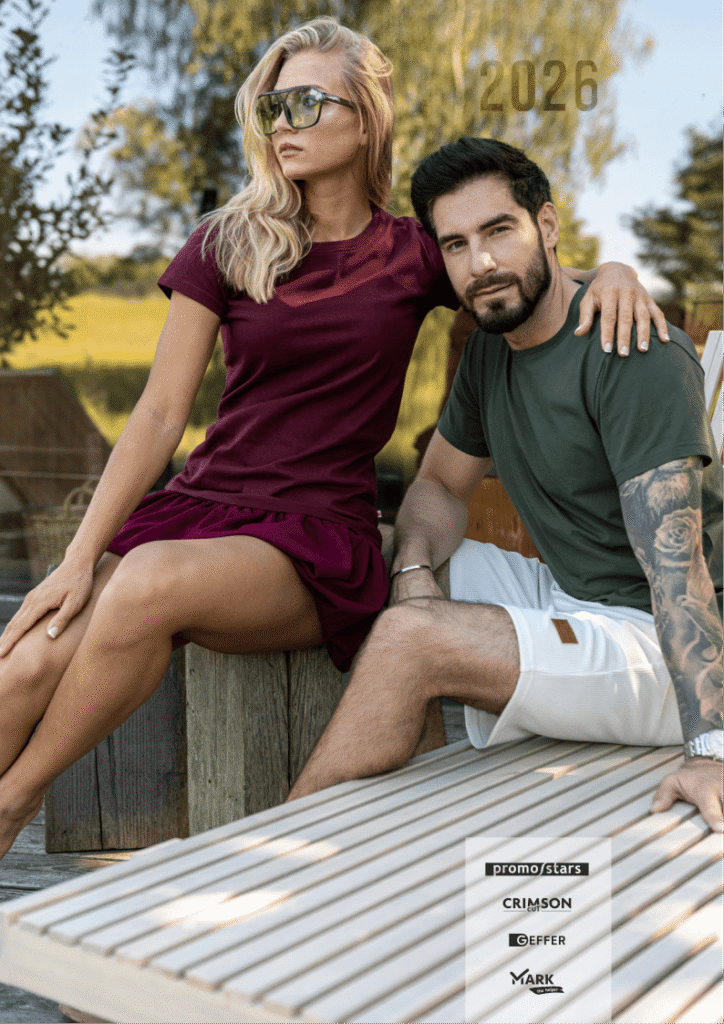 Couple posing outdoors on a wooden deck; woman in a burgundy dress and sunglasses, man in a green T-shirt and white shorts, with 2026 text and brand logos in the lower right corner.